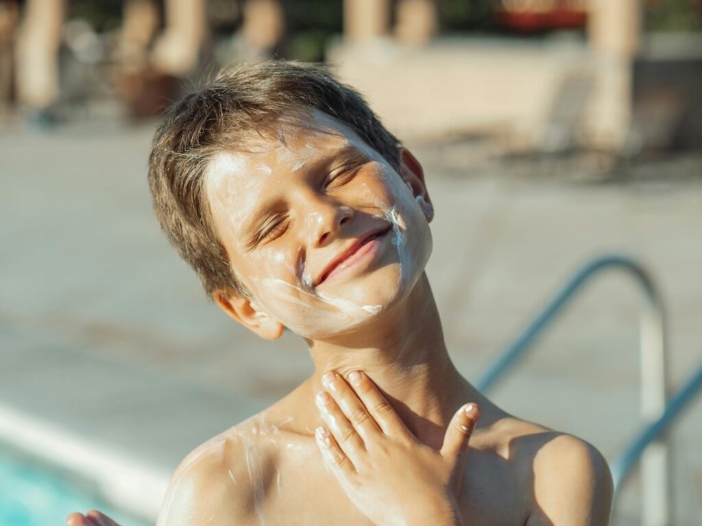 Smiling boy applying sunscreen, enjoying sunny day by the pool.